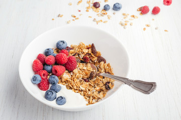 Granola with yogurt and berries in bowl on the white wooden table. Shot at angle.