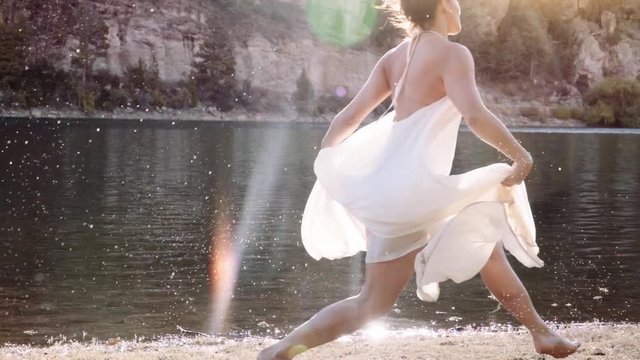 Classic ballerina wearing a bridal dress while dancing on the shore of the lake, Slow motion. Silhouette of bridal ballerina.