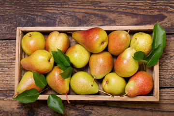 pears with leaves in a box on wooden table, top view