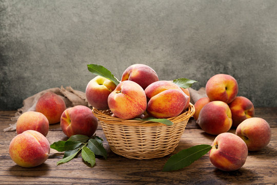 peaches with leaves in a basket on wooden table