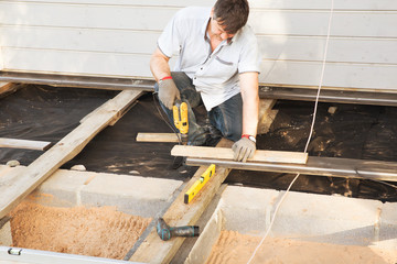 Man carpenter installing a wood floor outdoor terrace in new house construction site. Scandinavian style