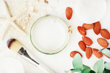 Glass Jar of natural cleansing skincare tonic closeup top view on white desk, homemade cosmetic product with rice and almond milk, light purity tones.