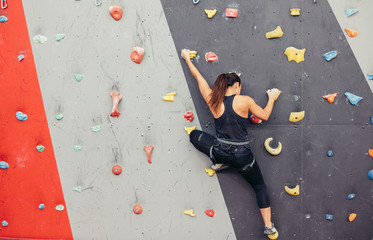 Back view of professional climber unrecognizable woman climbing on practical wall indoor, bouldering