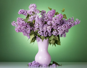 Luxurious bouquet of fragrant lilac in vase on green