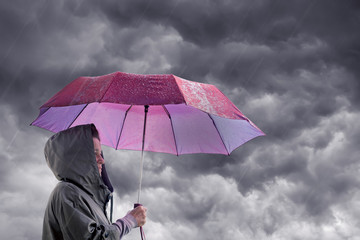 Woman with an umbrella against the background of a dark stormy sky. The woman is hiding under an umbrella from the rain. Protection from danger, natural disasters
