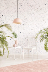 White chair between plants in pastel living room interior with lamp above carpet. Real photo