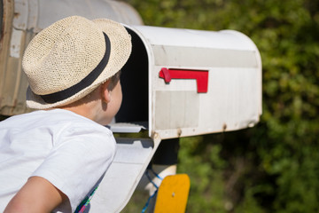 portrait of kid boy opening post box and looking for mail outdoors.