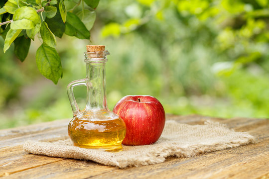 Apple vinegar in glass bottle and fresh red apple on wooden boards with green natural background