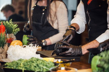 Cropped view of Chefs hands standing in raw at table and making hamburgers and burgers.