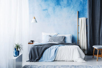 Grey and blue bedding on bed in spacious bedroom interior with ladder and plant - obrazy, fototapety, plakaty
