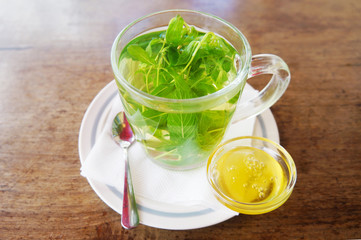 Cup of mint tea and small jar of honey on wooden table, side view 