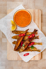 Roasted capelins with lemon and dip sauce on a wooden plate