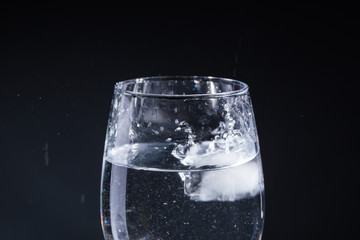 Glass of water on a gray background with drops in different directions