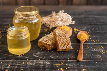 Beautiful transparent honey in bank, honeycombs and pollen on a wooden table. It can be used as a background