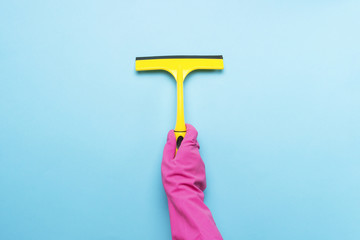 Female hand in pink gloves holding a scraper for cleaning windows on a blue background. cleaning service concept. Flat lay, Top view