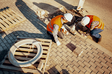High angle of physical workers in reflective vests arranging a paving stones