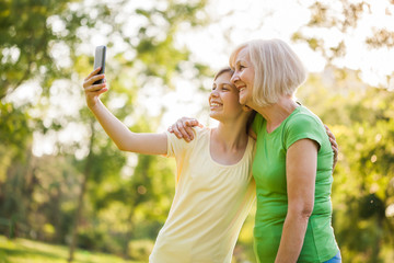 Grandmother and granddaughter are taking selfie in park. 