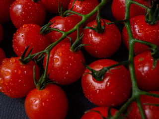 Tomatoes on black background. Branch with fresh cherry tomatoes. Ripe red tomatoes. 