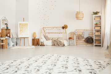 Big fluffy carpet placed on the floor in white Scandinavian style kid room interior with wooden furniture and home-shape bed © Photographee.eu