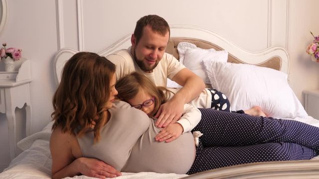 Pregnant woman mother with her family at home in bed, daughter and husband stroke the belly