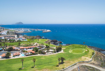Golf course and blue sea in luxurius beachfront hotel resort near atlantic ocean and yacht port. Green grass field, palm trees, house apartments, blue sky and ocean