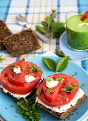 Belegte Bauernbrot-Scheiben mit Weichkäse und frischen Tomatenscheiben mit einem Glas Gemüse-Smoothie 