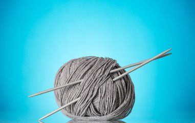 Skein of thick, grey yarn and knitting needles on blue