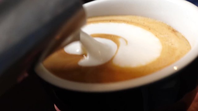 Close up of barista draws latte art making cappuccino in a cup of espresso coffee