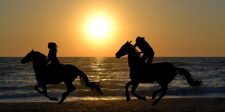 Two horse riders galloping on the beach