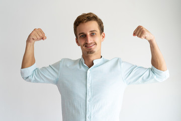 Focused guy in white casual shirt showing strength gesture. Handsome young Caucasian man posing and...