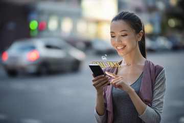 A young beautiful asian woman using innocative technology in her smart phone to call a taxi service. Communicate about transport, taxi, applications, being on the move, commuting, mobile internet