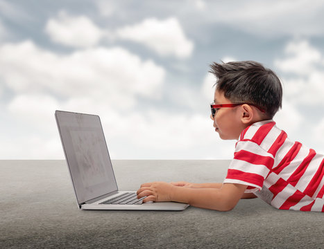 kid using a laptop computer with sky background.Asian boy wearing a red t-shirt and red pants wearing glasses is using a computer.concept idea