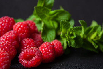 Raspberries with mint leaves on a black background.
