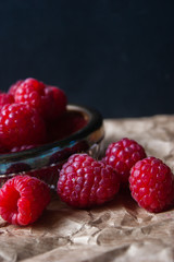 Raspberry berries in a glass plate on a black background.