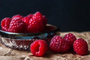 Raspberry berries in a glass plate on a black background.