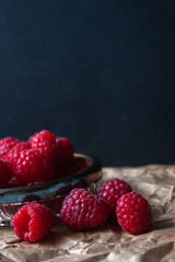 Raspberry berries in a glass plate on a black background.