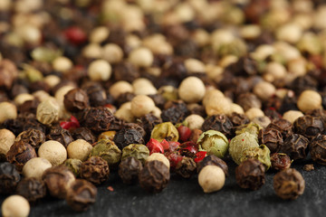 Extreme close up of a mix of black, red, green and white peppercorns on a black, rustic stone kitchen board. Shallow depth of field. Macro food texture background
