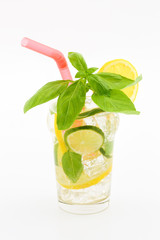 Fresh summer cocktail with lemon and limette slices, ice and basil leaves on a lighted background with red straw