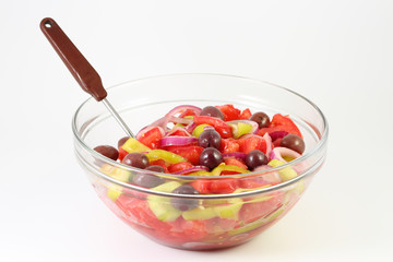 Fresh summer vegetable salad with tomatoes, cucumber, green pepper, red onion and olives in a glass bowl