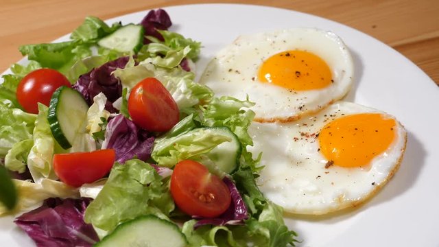 Chef cooking breakfast put two fried eggs on a plate with fresh vegetable salad