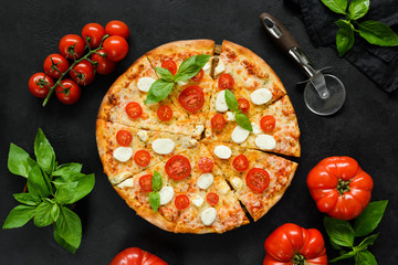 Homemade italian pizza with mozzarella, tomatoes and basil on black concrete backdrop. Sliced tasty...