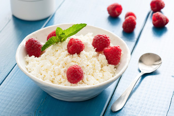 Ricotta, tvorog or cottage cheese with raspberries and honey on blue wooden table. Healthy summer...
