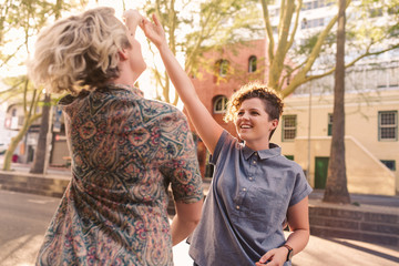 Smiling lesbian couple holding hands and dancing in the city