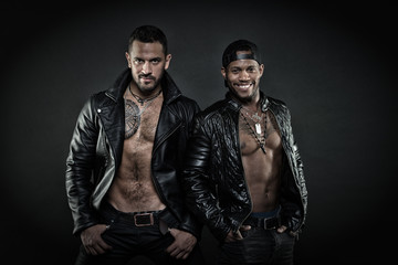 Leather masculine clothing concept. Men on smiling faces with bristle. Machos with muscular torsos look attractive in leather jackets, dark background. Men with sexy muscular torsos look brutally