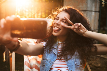 Young beautiful curly woman outdoors in park make selfie