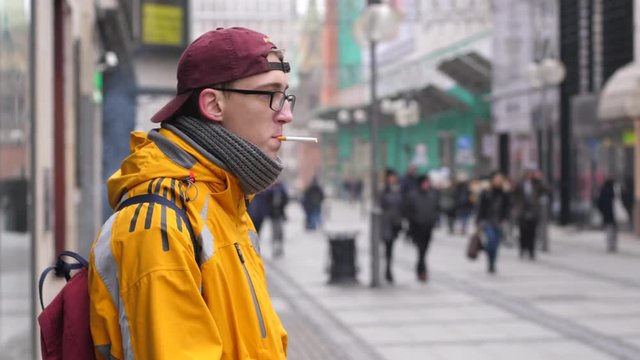 Smoking in public place young teenager guy staying on street with cigarette wearing yellow jacket