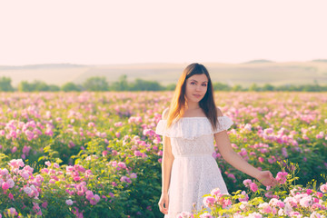Beautiful young woman posing near roses in a garden.