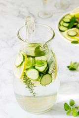 Lemonade with cucumber, lemon balm and thyme in a transparent jar on the background of plates with ingredients.