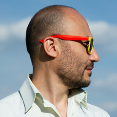 portrait of a businessman in modern sunglasses against a blue sky background.