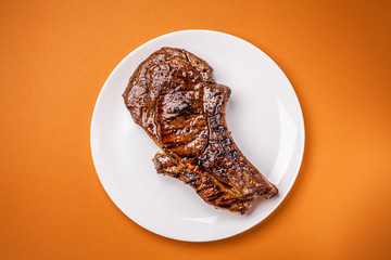 A large and juicy piece of roast lamb steak, veal, pork or beef lies on a white ceramic plate with spices, next to the fork and knife. Top view, copy space